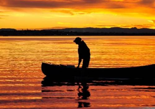 How to canoe solo - Silhouette of a man standing in a canoe at sunset